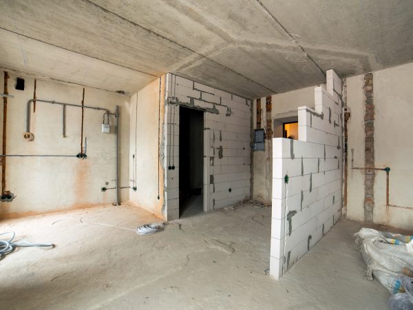 Interior of an apartment room with bare walls and ceiling under construction.
