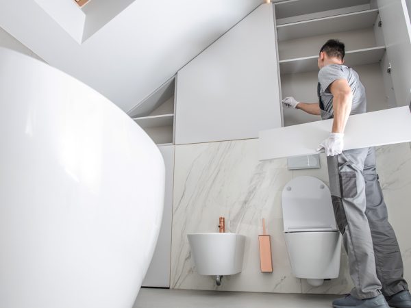 New Bathroom Interior Finishing. Caucasian Men in His 30s Assembling Modern Cabinets. Home Interior Remodeling Theme.